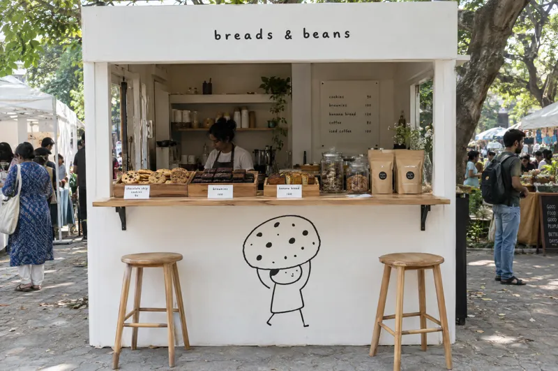 Concept of a white Breads and Beans pop-up stall with an oak counter and a cookie drawing